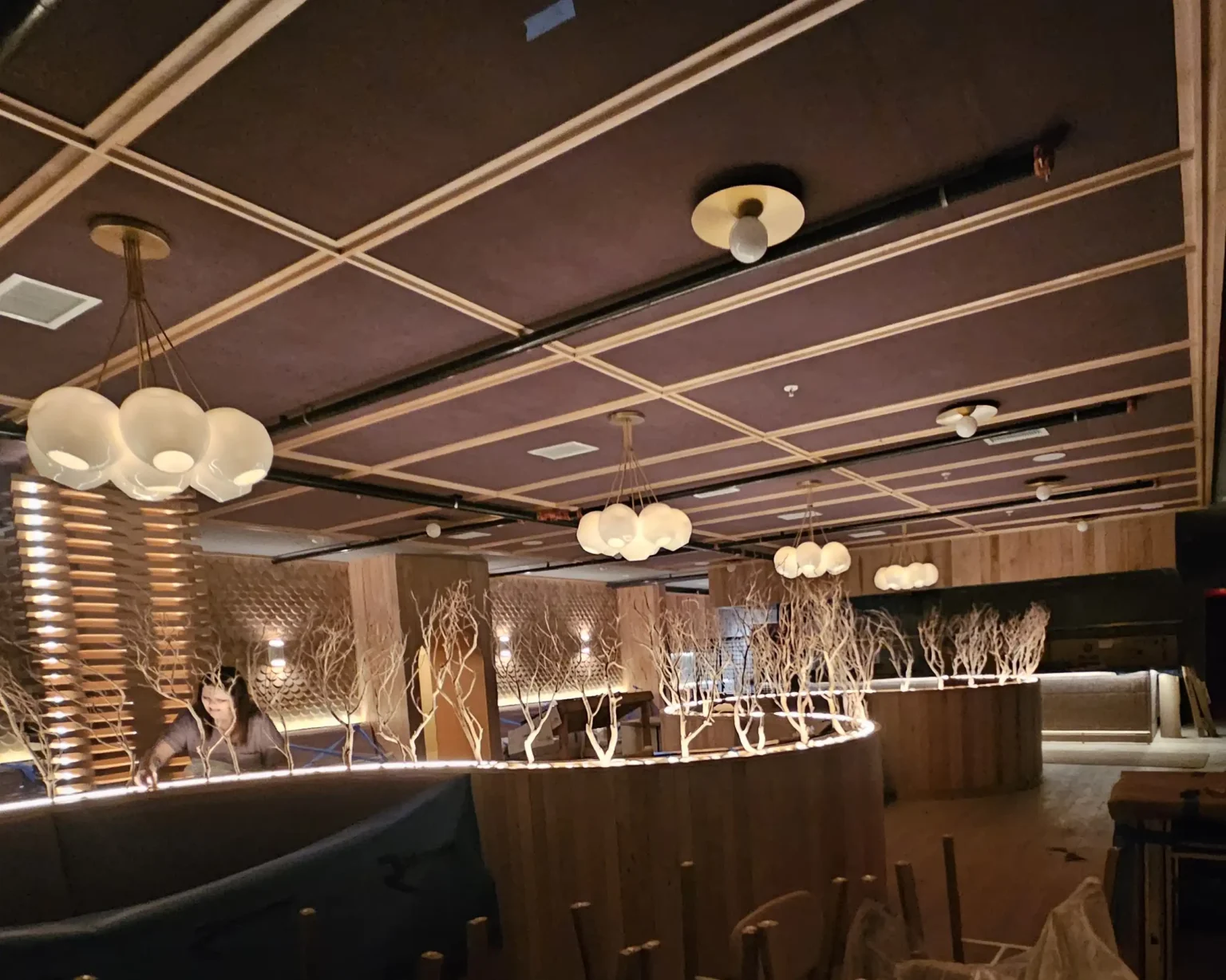 Sandblasted manzanita branch installation in custom restaurant booth dividers with warm ambient lighting and wood-paneled ceiling design